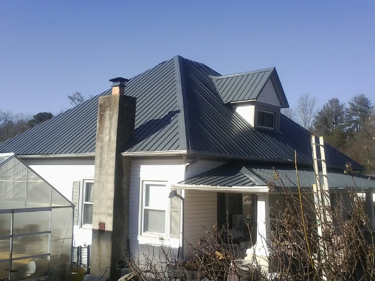 Dark blue standing seam metal roof on a white farmhouse with dormer — Slate & Tile Roof Repair by Roofing Brothers in Upton