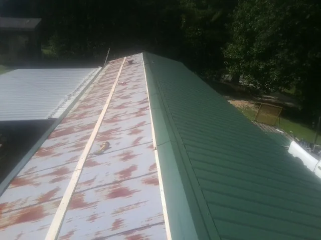 Old rusted panels beside newly installed green metal roofing — Wind Damage Roof Repair by Roofing Brothers in Upton