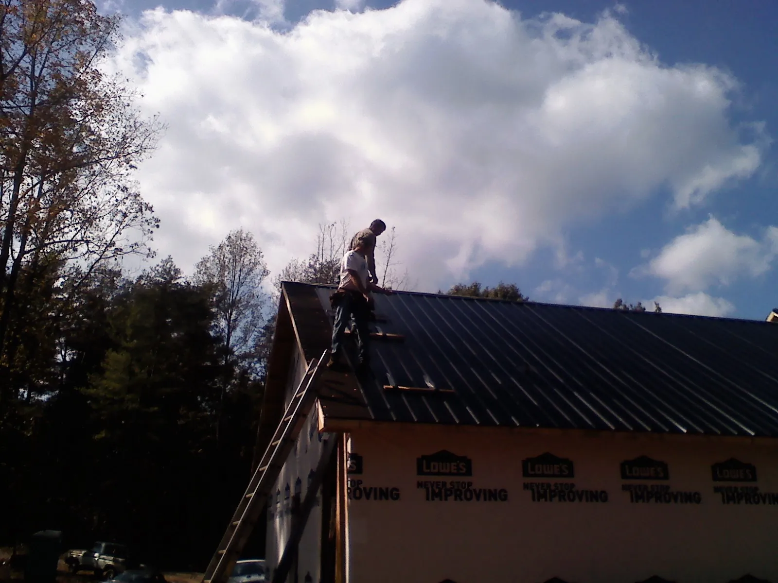Roofer fastening dark metal panels high against a cloudy sky, from a Roof Inspection job in Upton