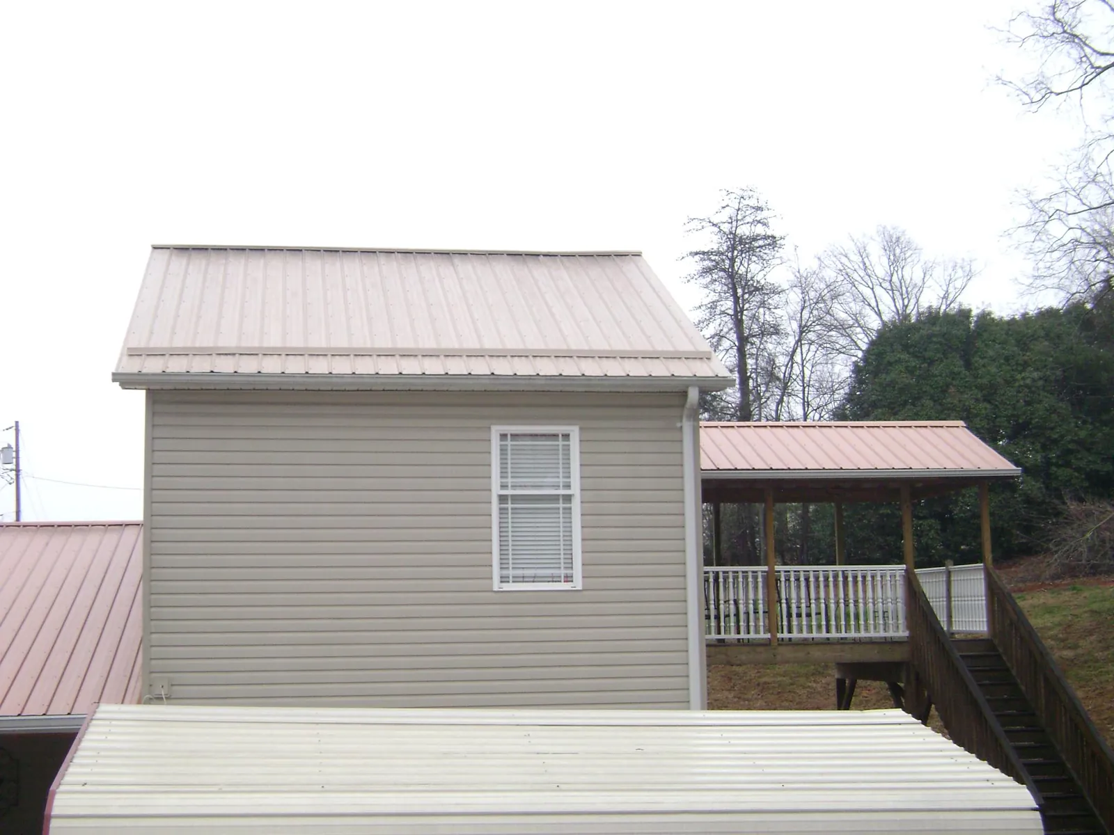 Tan metal roofs on a two story addition and attached porch, from a Roof Replacement job in Upton